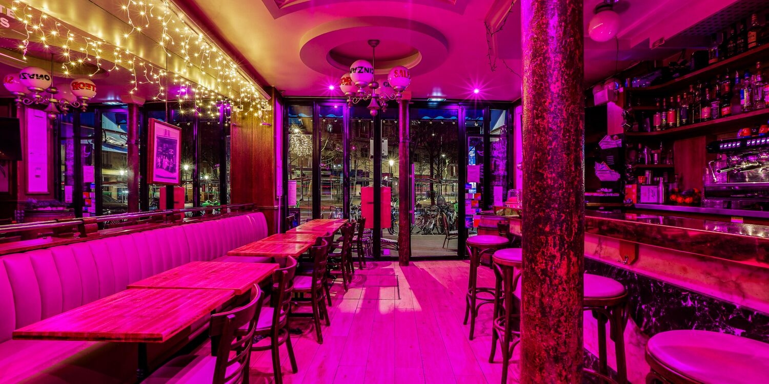 La salle de L'Horizon de nuit, ambiance néon rose, banquettes et tables en bois.